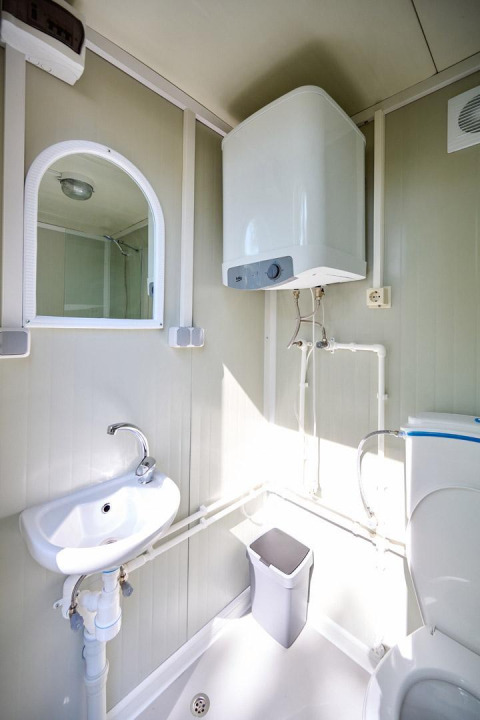 Baño en una tienda Villatent Compact con lavabo, espejo, inodoro, papelera y calentador de agua.