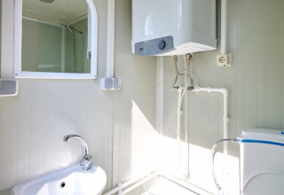Baño en una tienda Villatent Compact con lavabo, espejo, inodoro, papelera y calentador de agua.