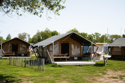 Tienda safari Villatent Compact + sanitary en un camping con césped, árboles y cielo despejado.