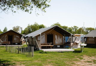 Tienda safari Villatent Compact + sanitary en un camping con césped, árboles y cielo despejado.