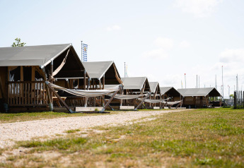 Safari tents Villatent Compact with private sanitary, lined up with hammocks on a sunny grassy area.