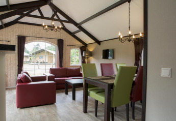 Lichte woonkamer in een natuurhuis met rode banken, groene eetstoelen en grote ramen naar buiten.