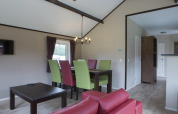 Salle à manger moderne dans une maison nature avec chaises colorées, table foncée et ambiance chaleureuse.