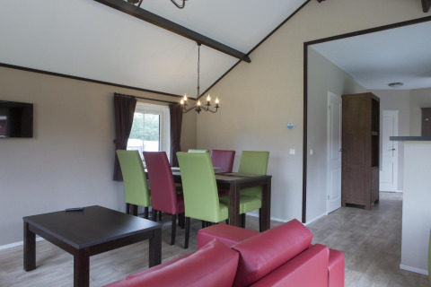 Modern dining area in a nature house with colorful chairs, dark table, and open layout leading to hallway.