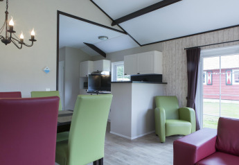 Sala de estar en una Nature house con sillas verdes y rojas, cocina moderna y grandes ventanales.