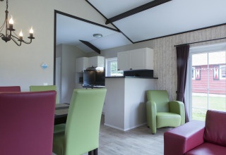 Woonkamer in een Nature house met groene en rode stoelen, moderne keuken en grote ramen met uitzicht.