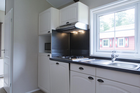 Cuisine moderne dans une maison nature avec meubles blancs, évier, plaque et vue sur un chalet extérieur.