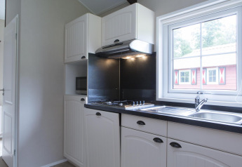 Modern kitchen in a nature house featuring white cabinets, a stove, sink, and window overlooking a cabin.