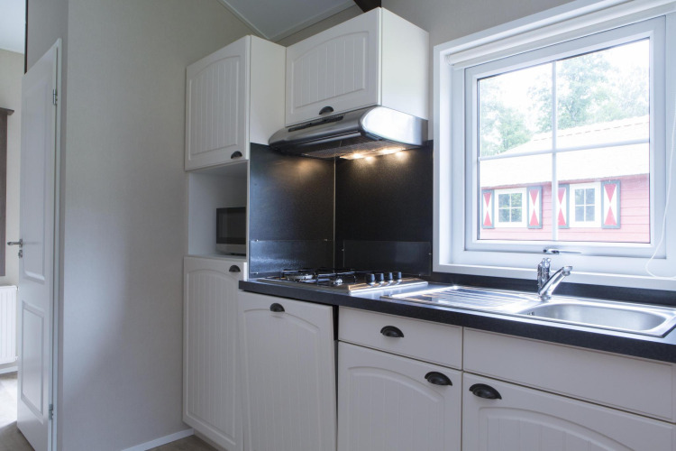 Modern kitchen in a nature house featuring white cabinets, a stove, sink, and window overlooking a cabin.