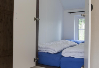 Gezellige slaapruimte in een natuurhuisje met blauwe lakens, witte dekbedden en zicht op de natuur.