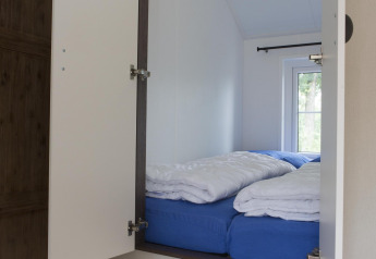 Bright sleeping nook in a nature house with blue sheets, white duvets and a window overlooking greenery.