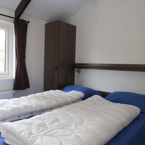 Bright bedroom in a nature house featuring two single beds with blue sheets and white duvets by a window.