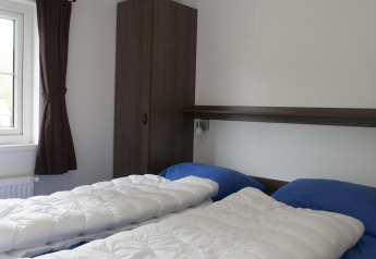 Bright bedroom in a nature house featuring two single beds with blue sheets and white duvets by a window.