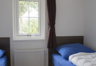 Habitación con dos camas individuales, ropa de cama azul, ventana con cortina oscura y radiador en casa natural.
