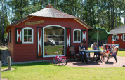 Maison nature rouge avec terrasse, trois femmes, une fille, un vélo rose et un grand parasol vert.