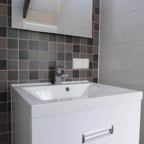 Lavabo de baño moderno con azulejos grises cuadrados, espejo grande y grifo cromado elegante.