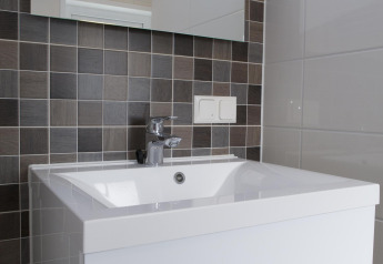 Lavabo da bagno moderno con piastrelle quadrate grigie, specchio grande e rubinetto cromato.