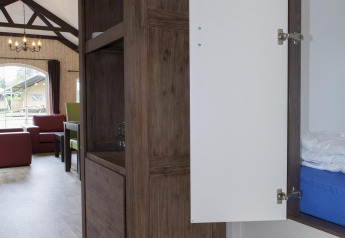 Interior of a nature house showing an open cabinet, sofas, and a large window with a garden view.