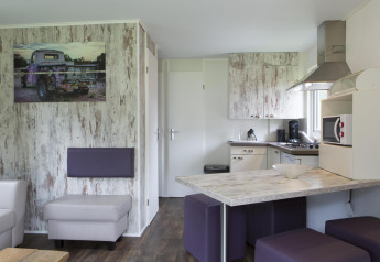 Moderne lodge med åbent køkken, spiseområde og stue i skandinavisk stil på Veluwecamping De Pampel.