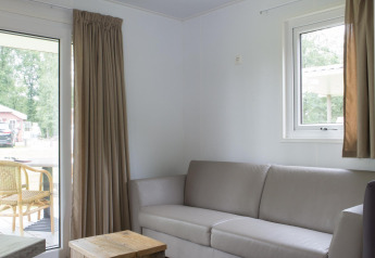 Stue i en Forest lodge på Veluwecamping De Pampel i Holland med sofa, træbord og udsigt til terrassen.
