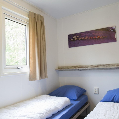 To enkeltsenge med blå betræk og et vindue i et lyst værelse i Forest lodge på Veluwecamping De Pampel.