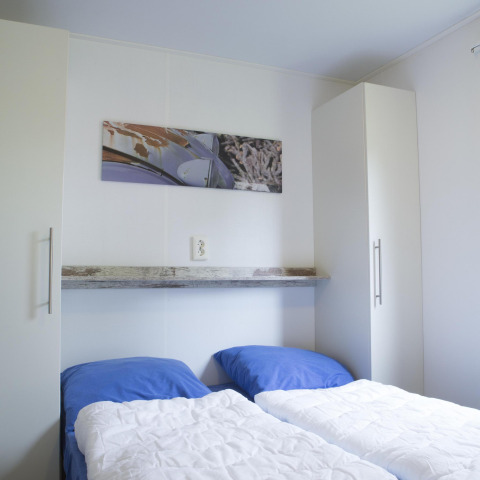 Dormitorio con dos camas individuales, almohadas azules y armarios blancos en Forest lodge de Veluwecamping De Pampel.