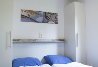 Dormitorio con dos camas individuales, almohadas azules y armarios blancos en Forest lodge de Veluwecamping De Pampel.
