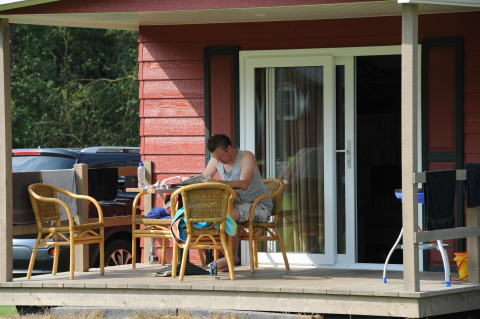 Hombre sentado en el porche de una cabaña Forest lodge en Veluwecamping De Pampel, Países Bajos.