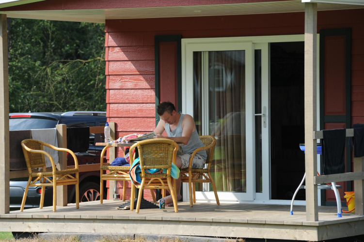 Man sitting on the porch of a Forest lodge at Veluwecamping De Pampel in the Netherlands, relaxing.