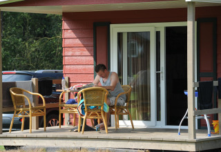 Mann sitzt auf der Veranda einer Hütte im Forest Lodge bei Veluwecamping De Pampel, Niederlande.