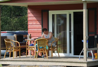Mann sitzt auf der Veranda einer Hütte im Forest Lodge bei Veluwecamping De Pampel, Niederlande.