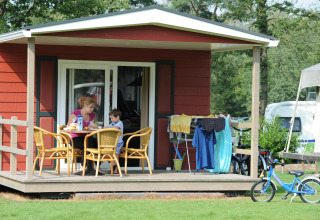 En mor og søn nyder morgenmad på terrassen ved en Forest Lodge på Veluwecamping De Pampel, Holland.