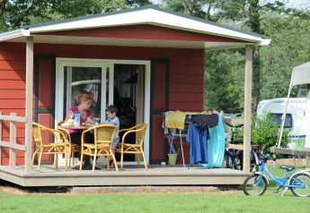 En mor og søn nyder morgenmad på terrassen ved en Forest Lodge på Veluwecamping De Pampel, Holland.