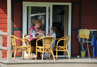 Een vrouw en kind ontbijten op de veranda van Forest Lodge op Veluwecamping De Pampel in Nederland.