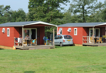 To røde hytter i skoven ved Forest Lodge, Veluwecamping De Pampel, med folk på verandaerne.