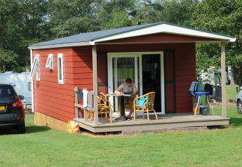 Rød lodge med veranda og mand ved bordet, Forest lodge ved Veluwecamping De Pampel i Holland.