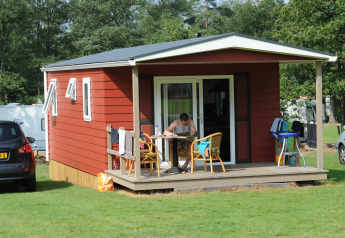 En person sidder ved et bord på verandaen til en rød lodge i Forest lodge ved Veluwecamping De Pampel.