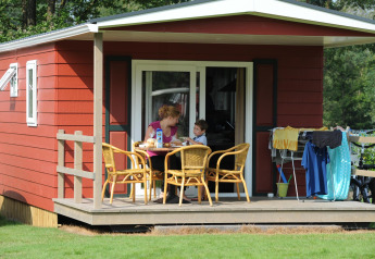 Family enjoys breakfast on the porch of Forest Lodge at Veluwecamping De Pampel in the Netherlands.