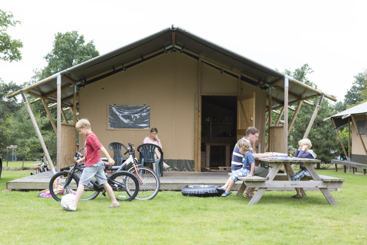 Family relaxing outside a Woodlodge safari tent. Children play with bikes while others sit at a picnic table.