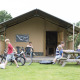 Family relaxing outside a Woodlodge safari tent. Children play with bikes while others sit at a picnic table.