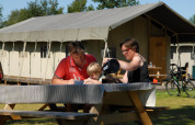 Familia desayunando al aire libre en una mesa de picnic frente a una tienda safari llamada Woodlodge.