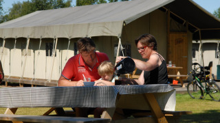 Familia desayunando al aire libre en una mesa de picnic frente a una tienda safari llamada Woodlodge.