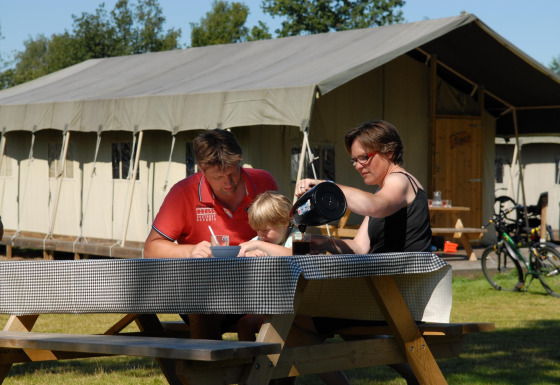 Familia desayunando al aire libre en una mesa de picnic frente a una tienda safari llamada Woodlodge.