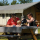 Familia desayunando al aire libre en una mesa de picnic frente a una tienda safari llamada Woodlodge.