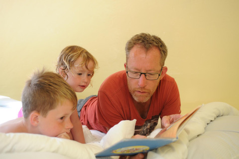Een man leest een boek voor aan twee kinderen op een bed in de Dreaming in a Dragon's Egg-pod in Nederland.