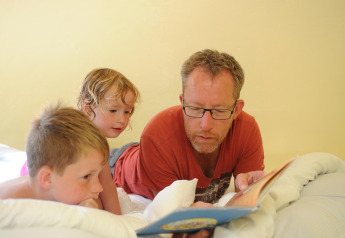 Een man leest een boek voor aan twee kinderen op een bed in de Dreaming in a Dragon's Egg-pod in Nederland.