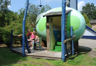 Familia sentada fuera de la cápsula Dreaming in a Dragon's Egg en Veluwecamping 't Schinkel, Países Bajos.
