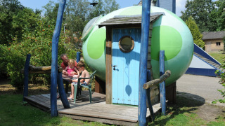 Famiglia rilassata accanto al pod Dreaming in a Dragon's Egg al Veluwecamping 't Schinkel, Paesi Bassi.