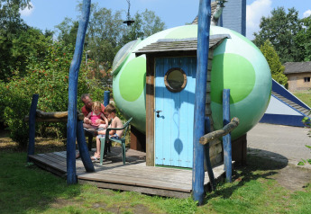 Famille assise devant le pod Dreaming in a Dragon's Egg au Veluwecamping 't Schinkel, Pays-Bas.