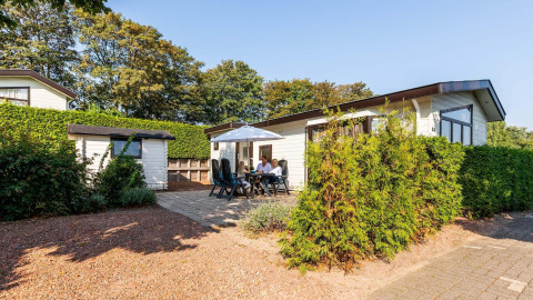 Feriehytte ved EuroParcs Noordwijkse Duinen i Holland med mennesker der nyder terrassen i solskin.